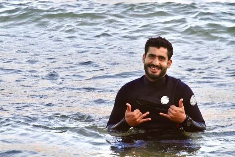 Ahmed souriant dans l’eau et faisant le signe shaka.