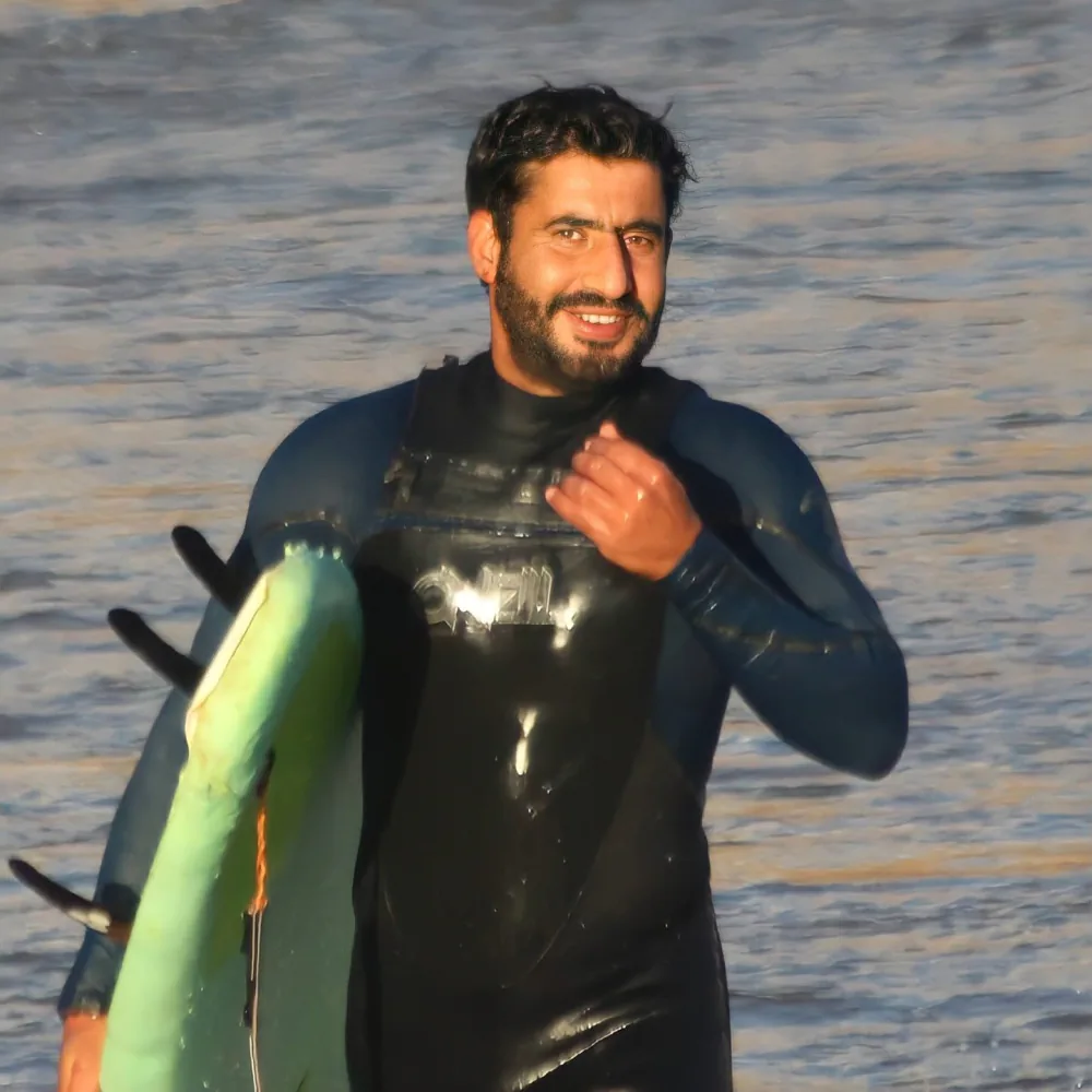 Ahmed souriant sur la plage d’Imsouane avec sa planche de surf.
