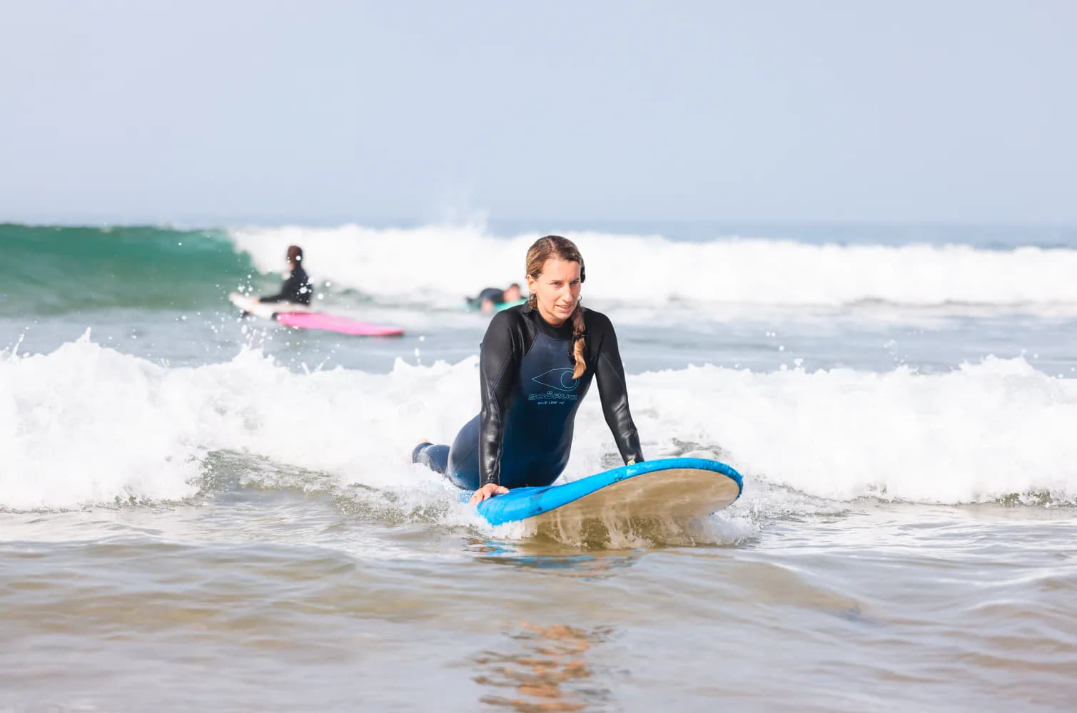 Une débutante ramant sur une planche en mousse bleue dans le shore break.