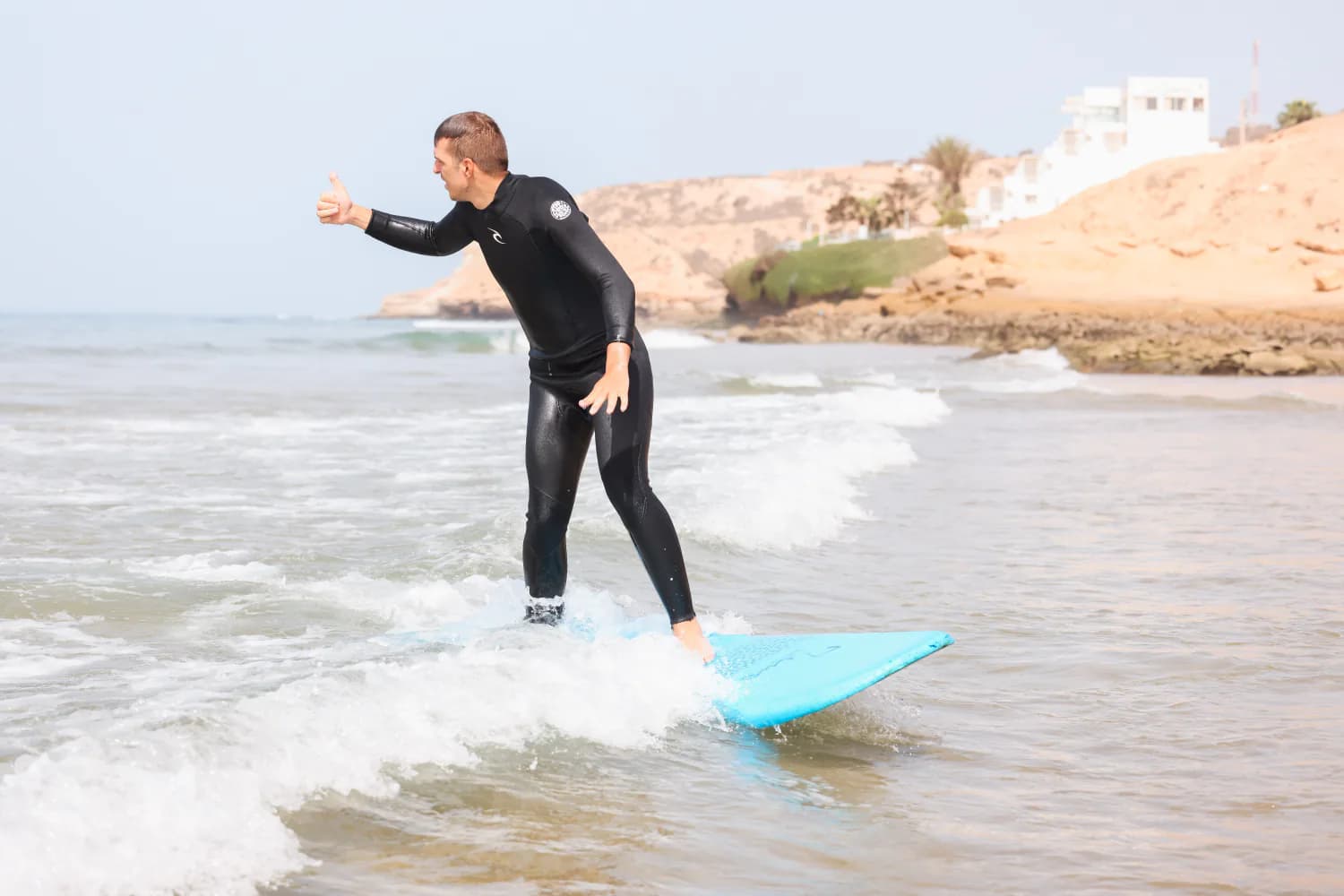 Un débutant surfant une petite vague, les deux bras tendus.