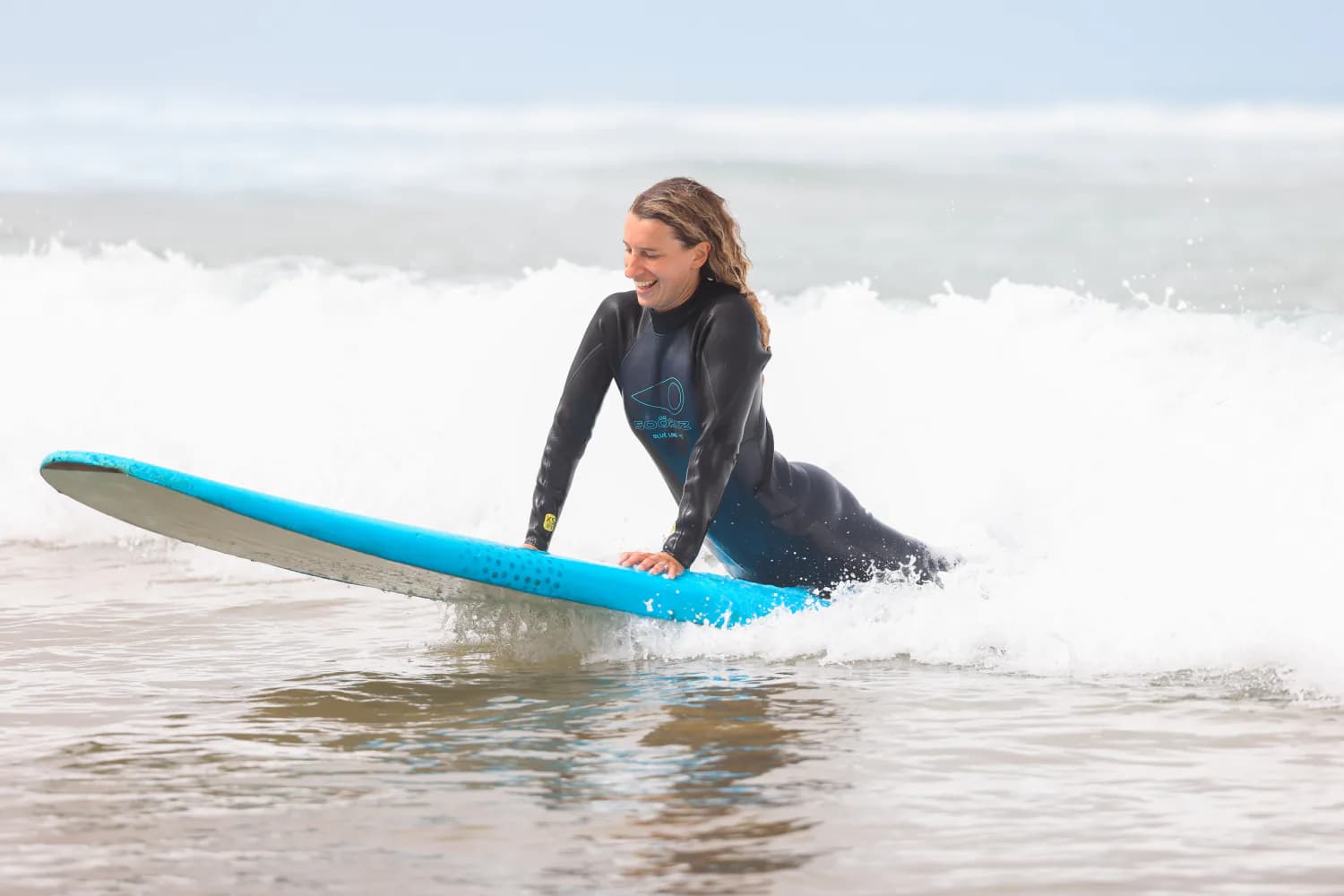 Un surfeur assis sur le sable avec une planche bleue après une session.
