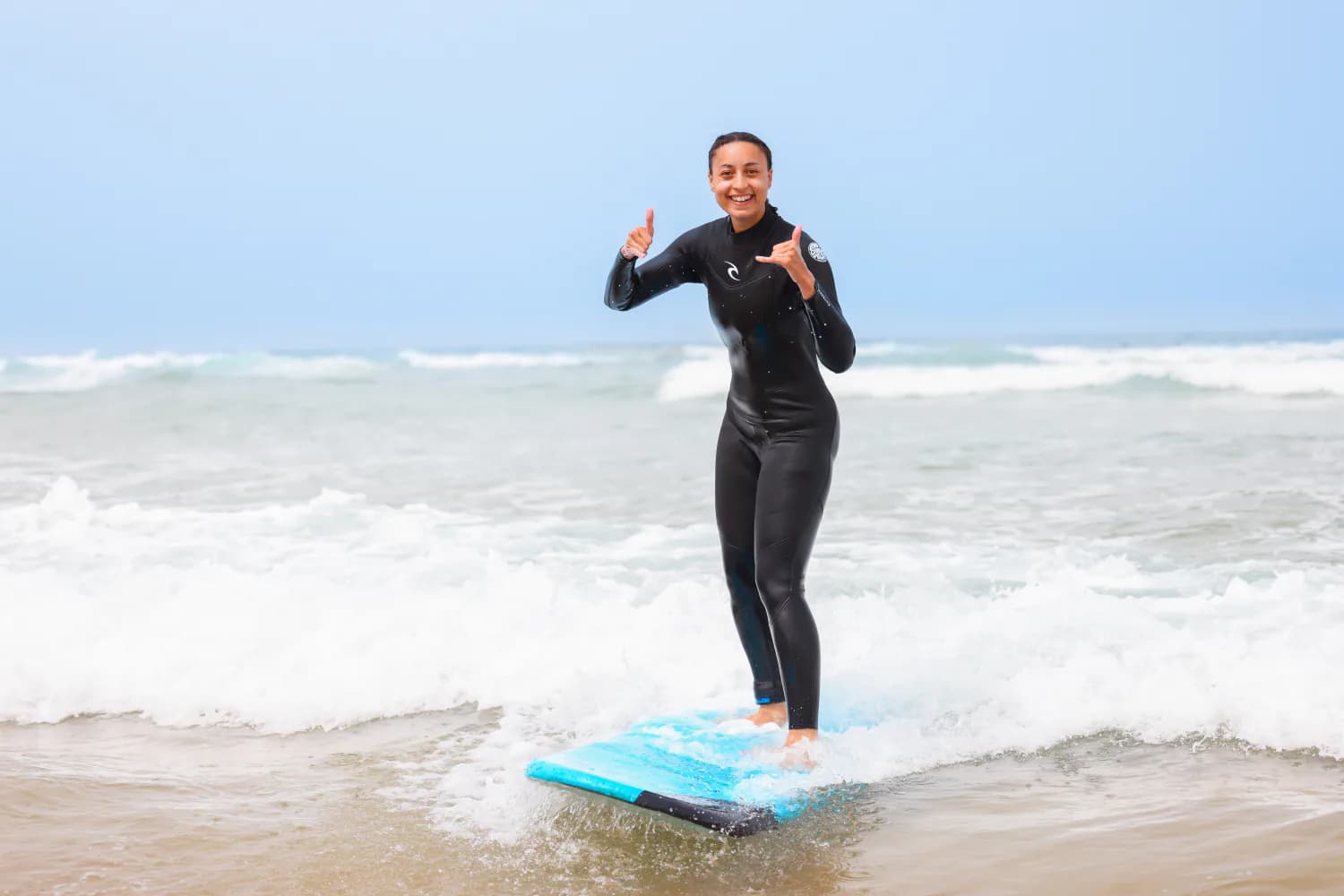 Un débutant debout sur une planche bleue près du rivage.