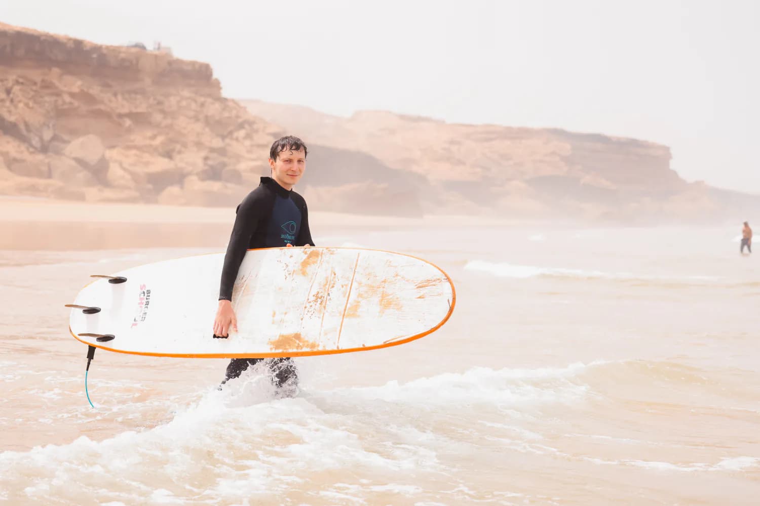 Un surfeur portant un longboard blanc dans les hauts-fonds.