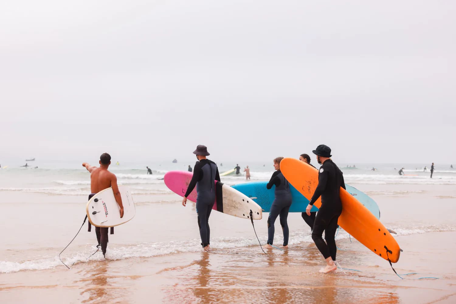 Quatre surfeurs portant des planches colorées vers l’eau au pied des falaises.