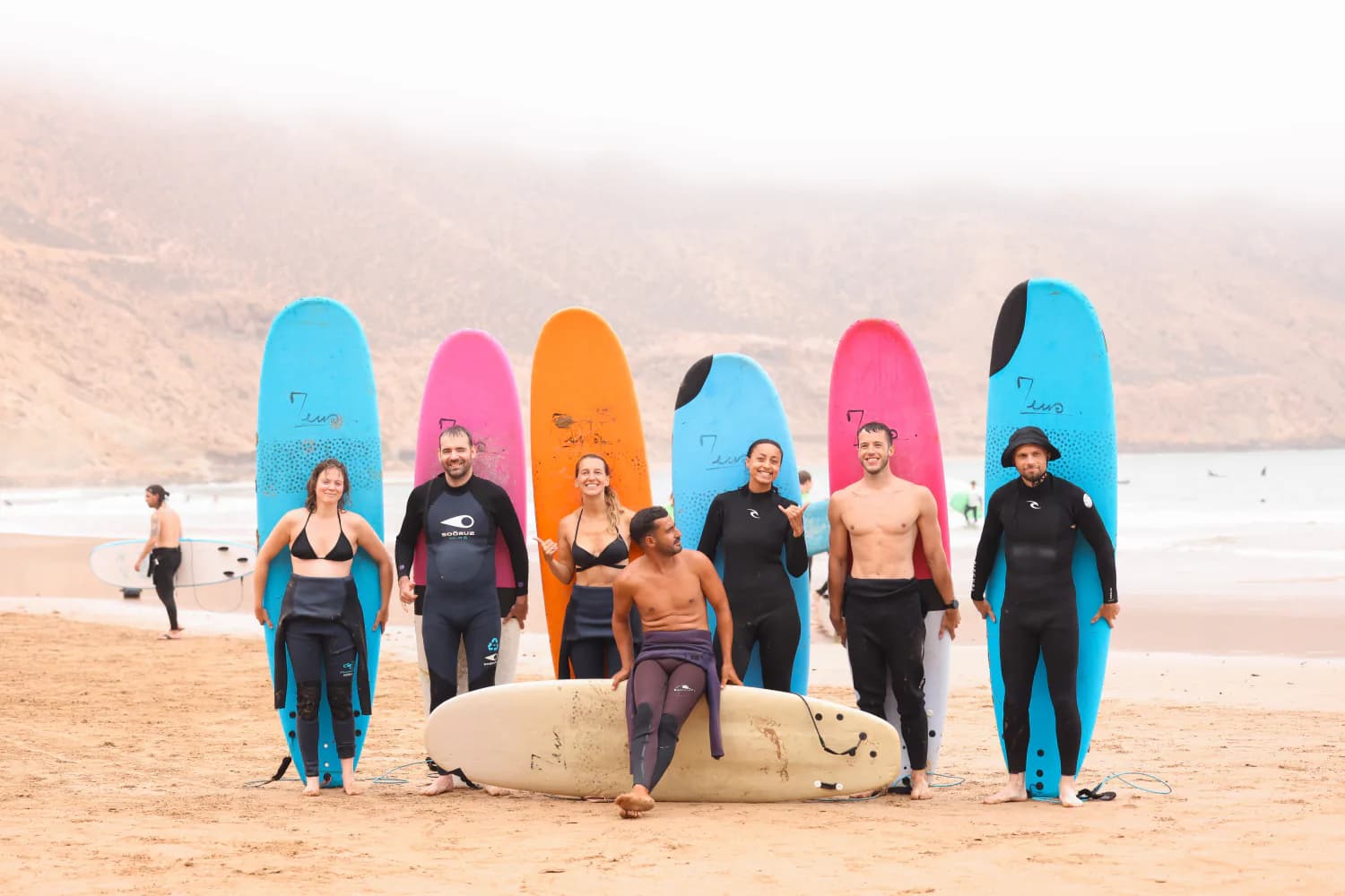 Un groupe de cours posant avec des planches colorées sur la plage.