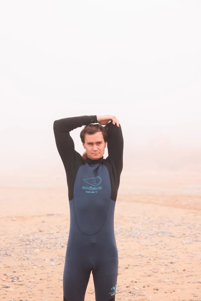 Un surfeur étirant son épaule avant d’entrer dans l’eau.
