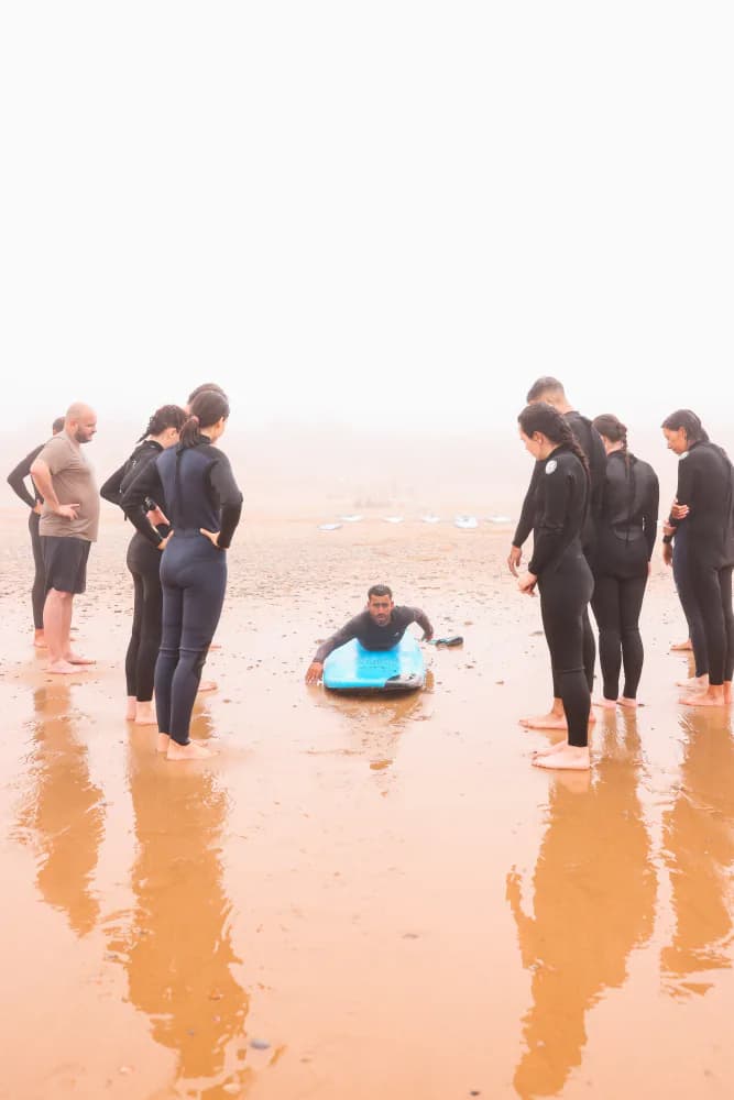 Un moniteur montrant la position de rame à un cercle d’élèves sur le sable mouillé.