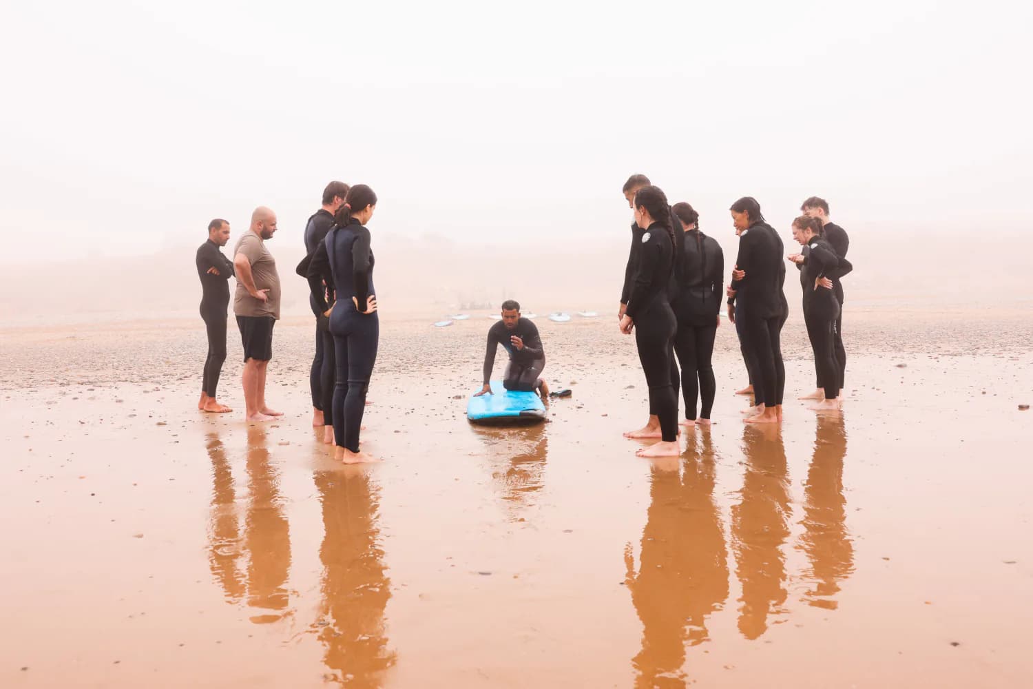 Des élèves écoutant leur moniteur à côté de planches bleues sur la plage.