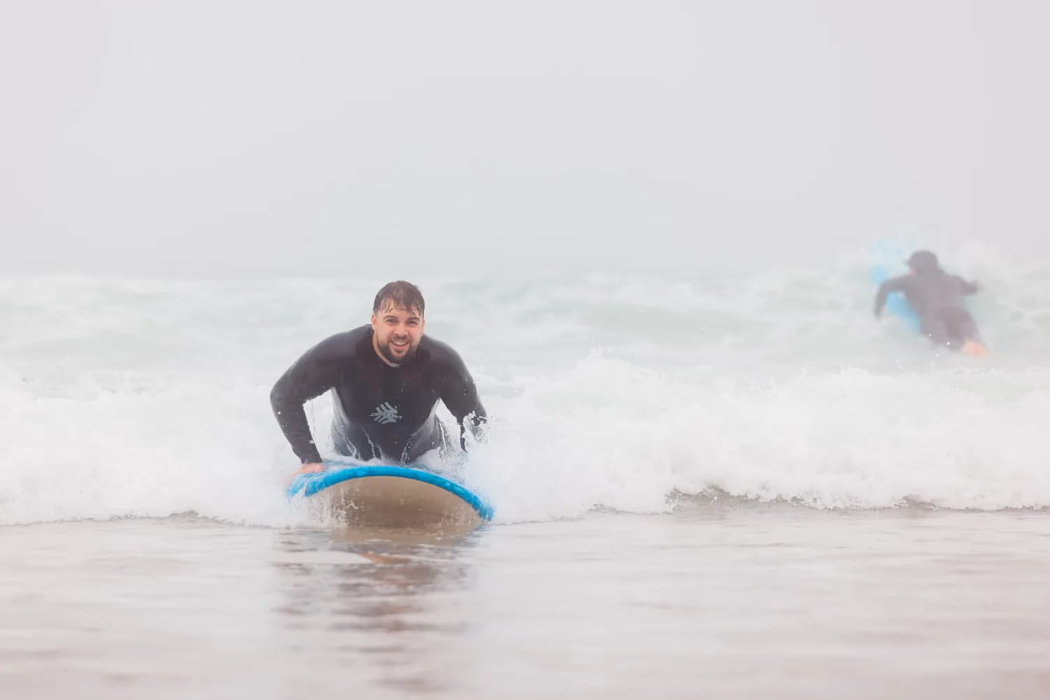 Une débutante souriante ramant sur une planche bleue dans la mousse.
