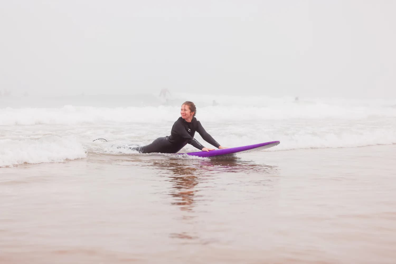 Un surfeur portant une planche en mousse bleue sur le sable mouillé.